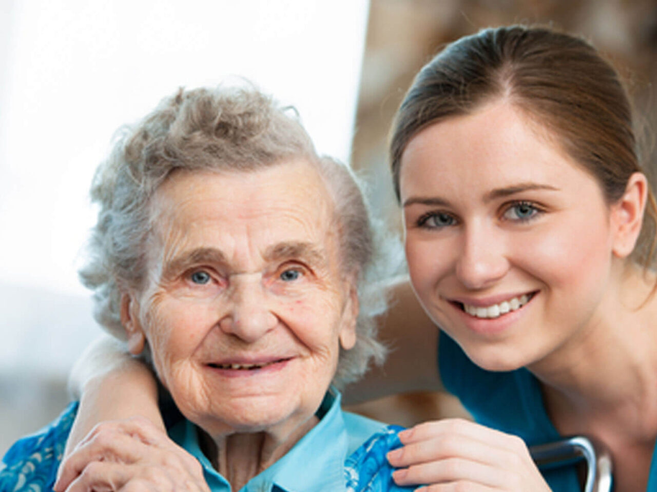 Elderly woman in wheelchair and young caretaker smiling
