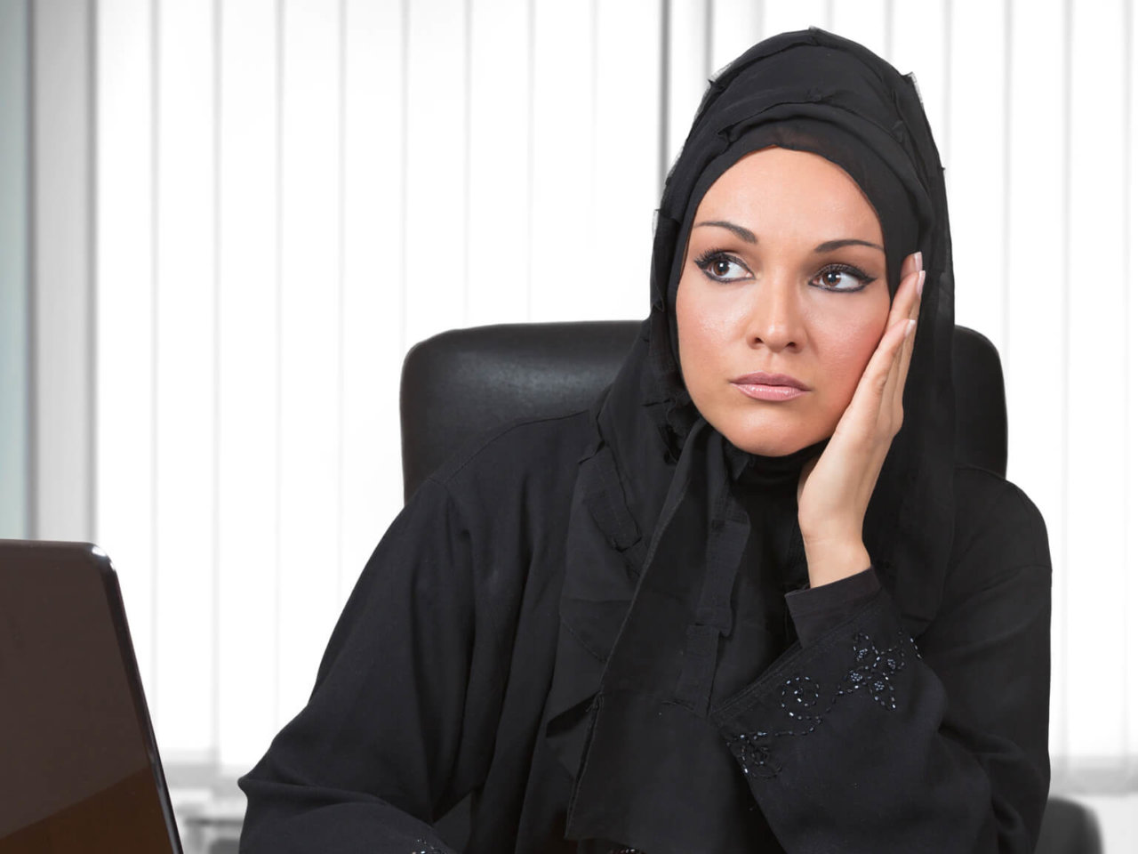 Business woman in head scarf thinking in front of computer