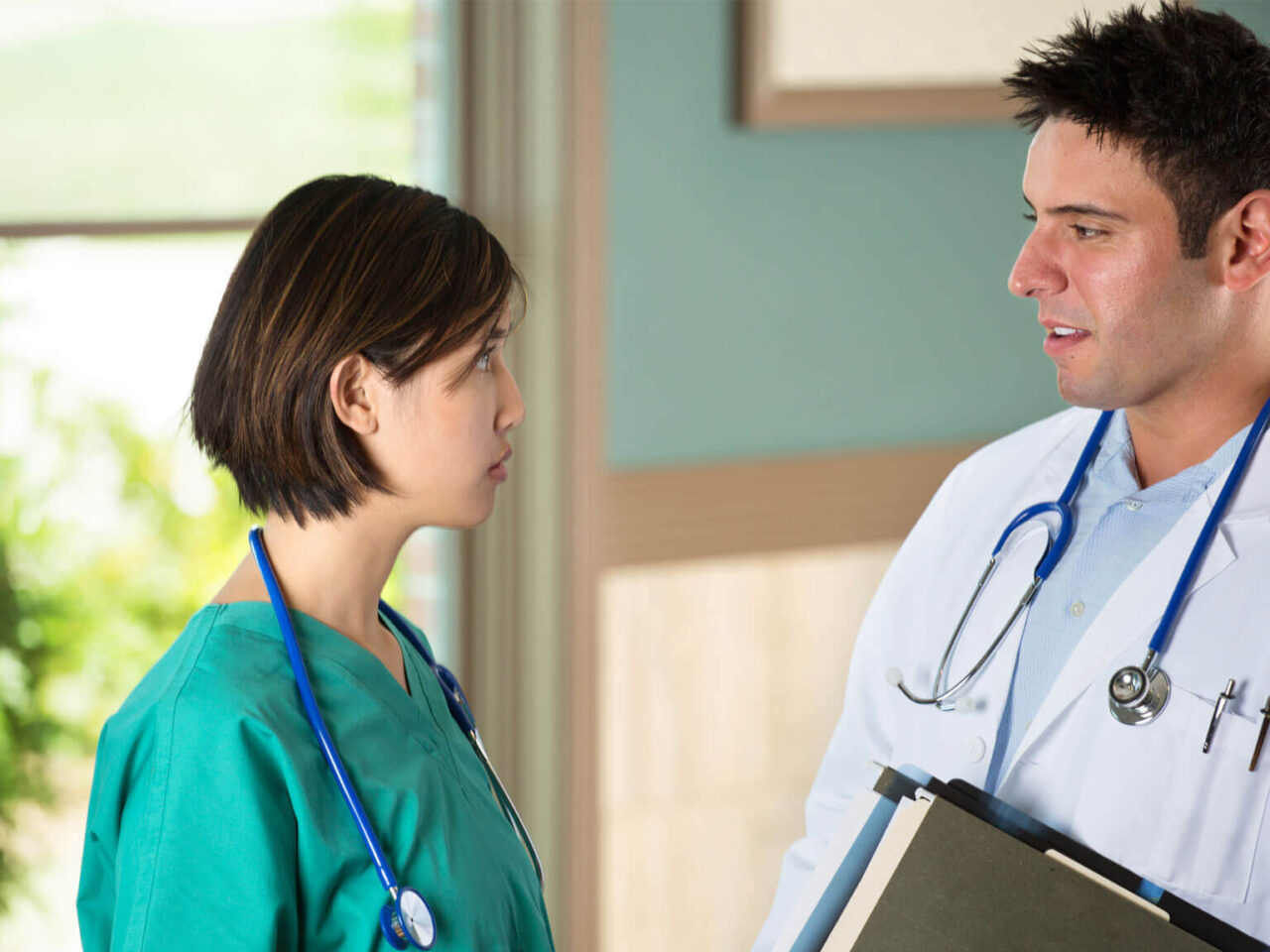 Male doctor and female doctor talking in a green hallway