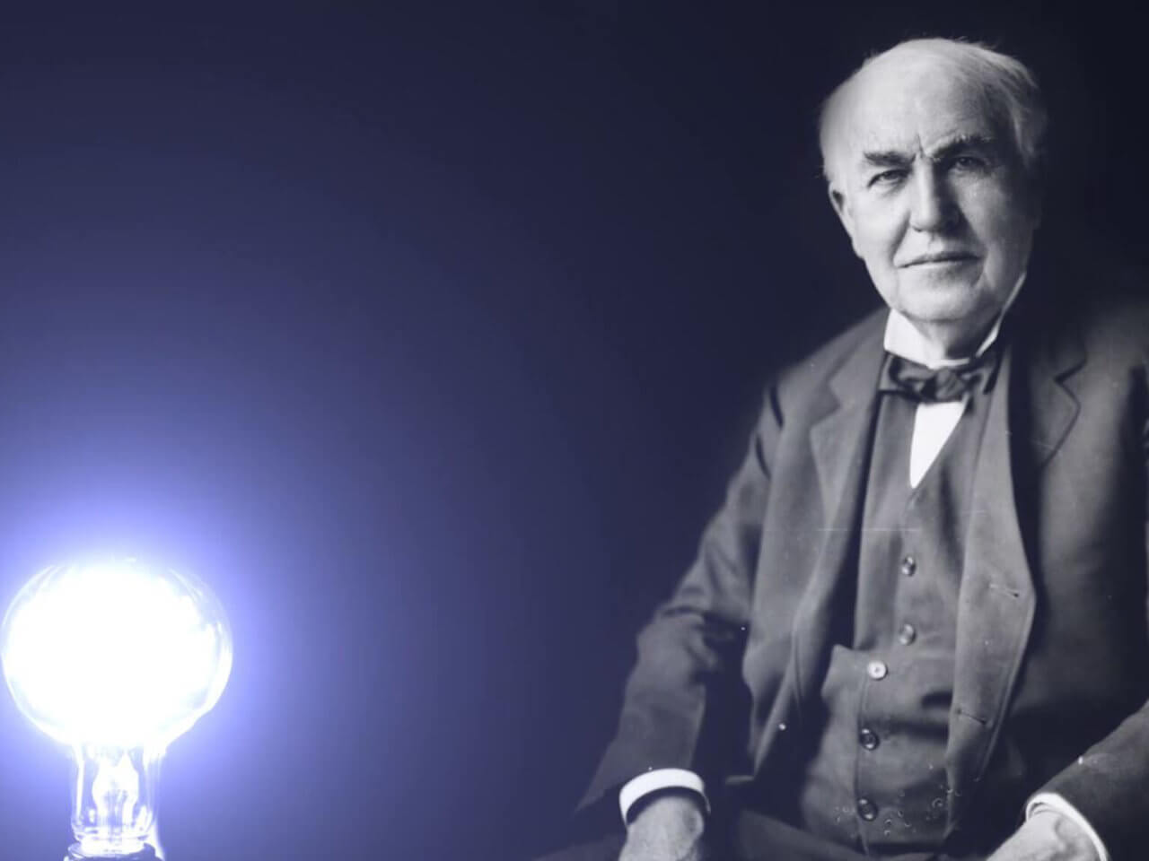 Thomas Edison sitting behind a bright lightbulb