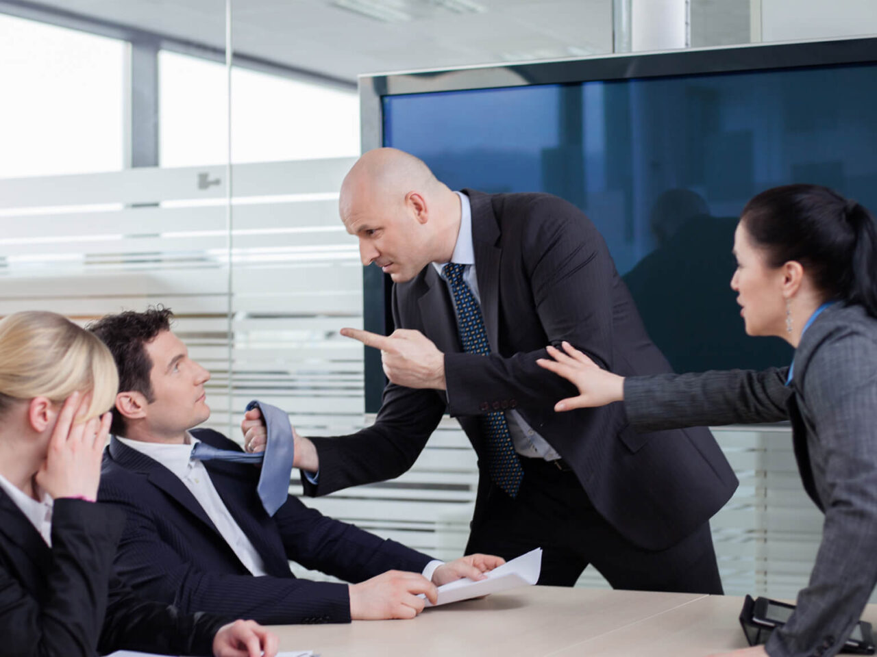 Businessman threatening colleague while other coworkers attempt to hold him back